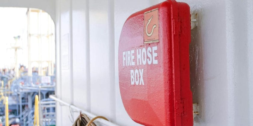 Close-up of a bright red fire hose box on a ship deck, emphasizing safety.