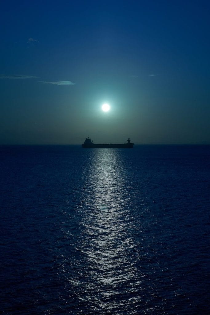 The sun is setting over the ocean with a ship in the distance