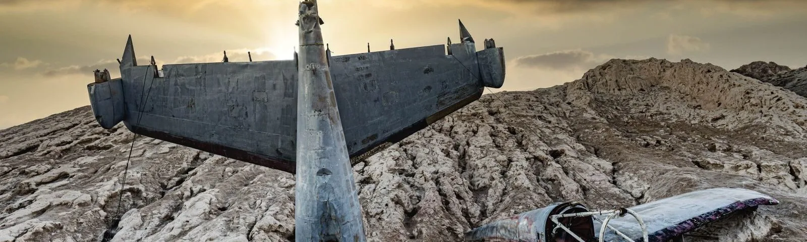 Dramatic sunset illuminating a crashed aircraft in a barren desert landscape.