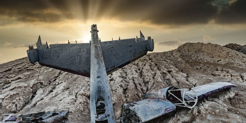 Dramatic sunset illuminating a crashed aircraft in a barren desert landscape.